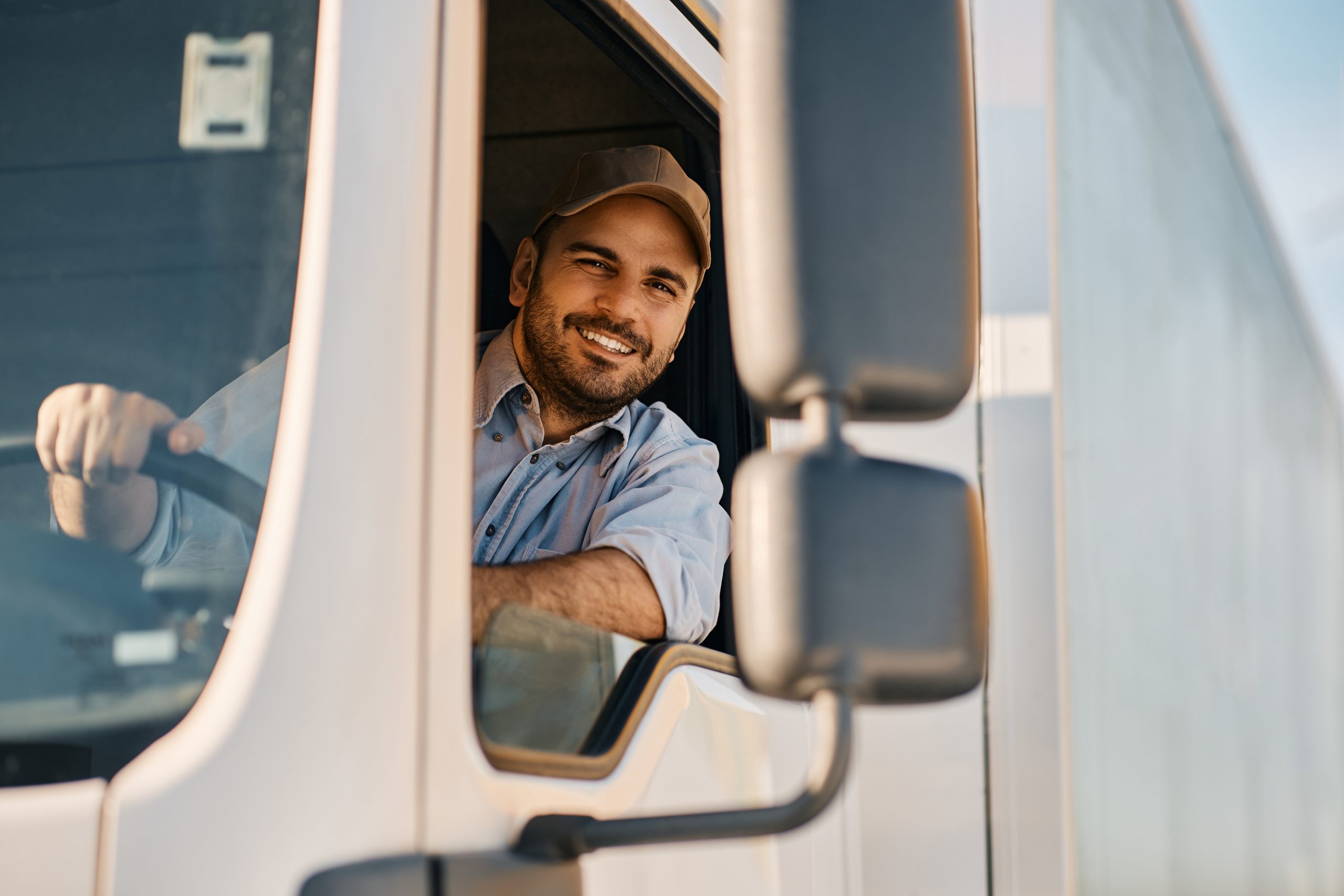 Professional truck driver inside his truck, smiling at the camera.